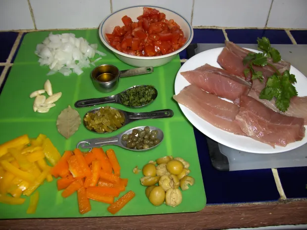 Overhead food prep station with chopped vegetables, spices in measuring spoons, and raw fish fillets, soft warm light