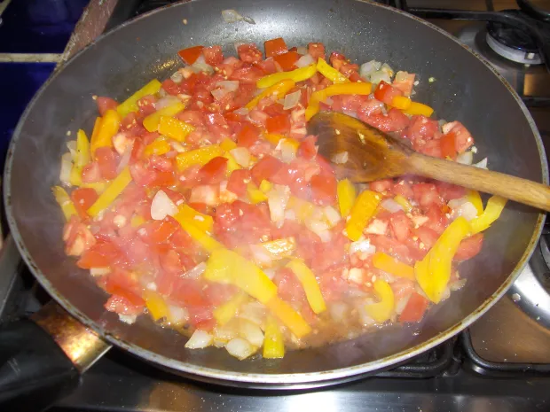 Bright, airy overhead view of diced red tomatoes, yellow peppers, and onions cooking in a dark skillet, with warm red and yellow colors and a calm, inviting mood